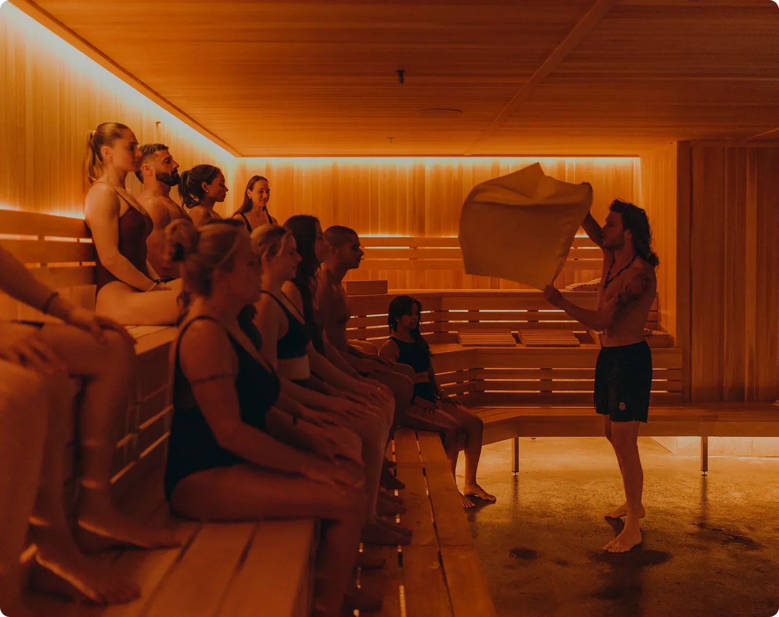 A JOY guide waving a towel over guests seated in the warm cedar sauna